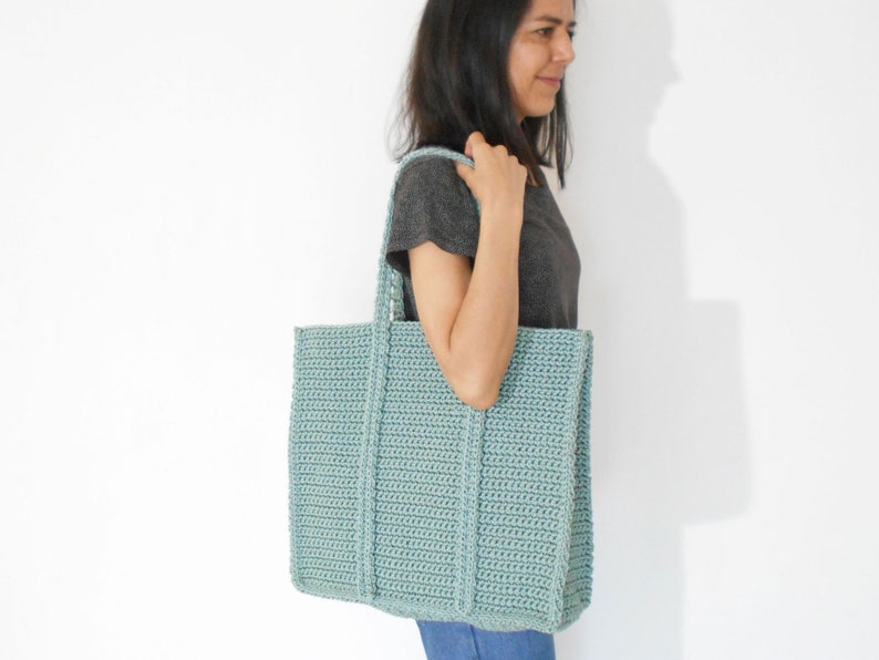 Op de afbeelding: Een lichtblauwe gehaakte tote bag met dikke hengsels. De tas is groot genoeg om dagelijkse benodigdheden te dragen.