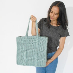 Op de afbeelding: Een lichtblauwe gehaakte tote bag met dikke hengsels. De tas is groot genoeg om dagelijkse benodigdheden te dragen.