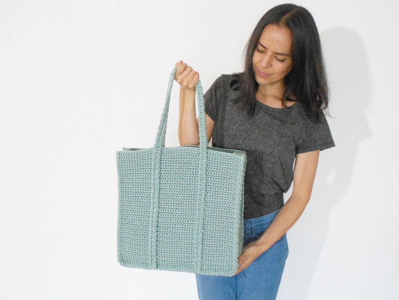 Op de afbeelding: Een lichtblauwe gehaakte tote bag met dikke hengsels. De tas is groot genoeg om dagelijkse benodigdheden te dragen.