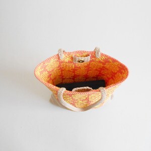 May include: A crocheted tote bag with a yellow and orange geometric pattern. The bag has a single button closure and two handles.