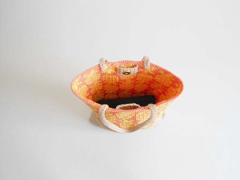 May include: A crocheted tote bag with a yellow and orange geometric pattern. The bag has a single button closure and two handles.