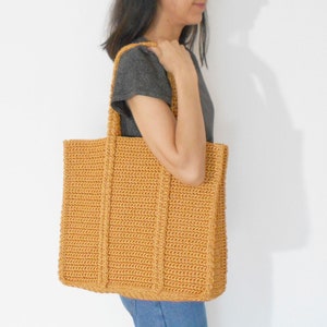 Op de afbeelding: Een grote, gehaakte tote bag in een mosterdgele kleur. De tas heeft een brede, platte basis en twee lange handvatten.