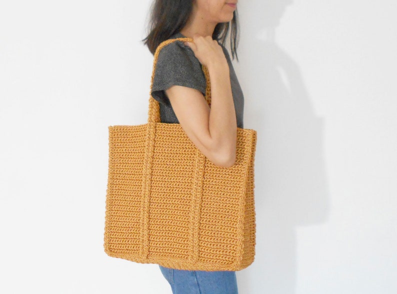 Op de afbeelding: Een grote, gehaakte tote bag in een mosterdgele kleur. De tas heeft een brede, platte basis en twee lange handvatten.