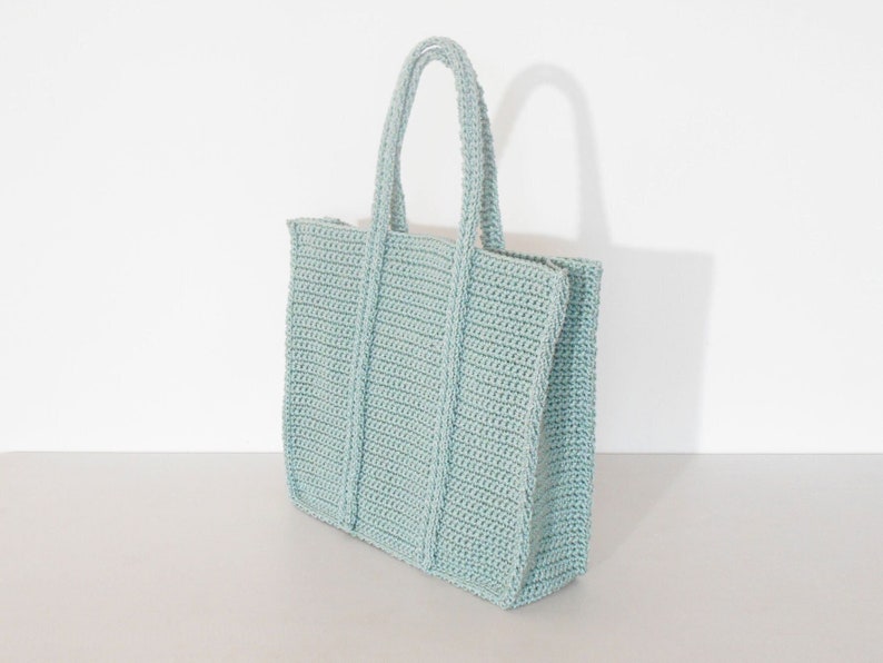Op de afbeelding: Een lichtblauwe gehaakte tote bag met een brede, rechthoekige vorm en twee handvatten.