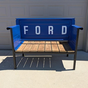 May include: A blue bench made from a Ford truck bed. The word "FORD" is displayed in white letters across the back. The seat is made of wooden planks, and the frame is black.