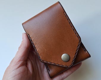 May include: A brown leather wallet with a snap closure and a stitched design. The wallet is folded in half and has a small pocket on the outside.