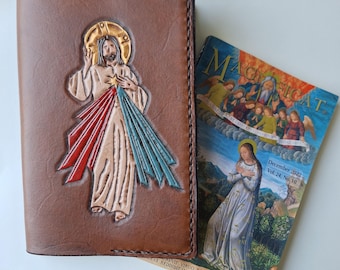 May include: Brown leather journal cover with an embossed image of Jesus with red and blue rays. Next to it is a magazine with the title "Magnificat" and the date "December 2022".