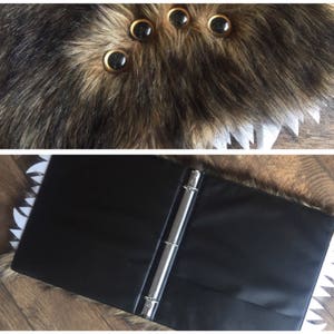 May include: A black three-ring binder with white jagged teeth on the edges. The binder is open and has a black interior. The binder is lying on a wooden surface.