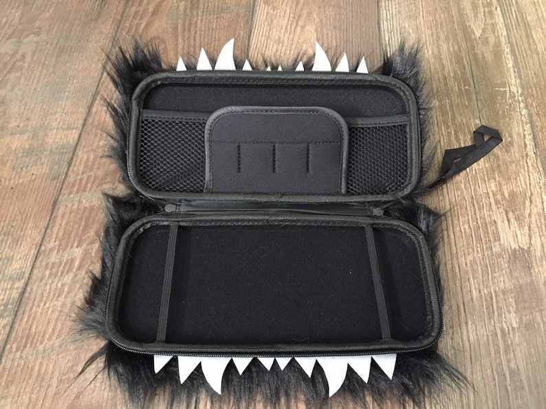 K&ouml;nnte beinhalten: Schwarze und wei&szlig;e, flauschige Tragetasche mit Rei&szlig;verschluss und einem Netzfach im Inneren. Die Tasche hat einen wei&szlig;en Kunststoffzahn-Design am Rand.