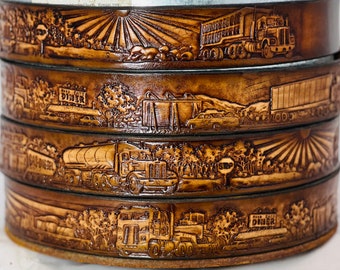 May include: A stack of five brown leather belts with embossed designs of trucks, diners, and landscapes. The belts are stacked on top of each other, with the top belt showing a truck driving through a field with a sunburst in the background.