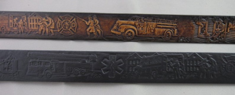 May include: Two leather belts with embossed designs. The top belt is brown with a fire truck and firefighters, and the text "FD" and "1955". The bottom belt is black with a fire truck and the text "Fire Department".
