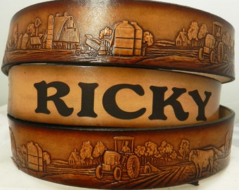 May include: A brown leather belt with a farm scene embossed on it. The belt has the name "RICKY" embossed on it.