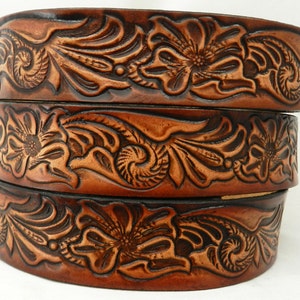 Może przedstawiać: Trzy brązowe skórzane paski z misternymi kwiatowymi zdobieniami. Paski są ułożone jeden na drugim, co pozwala zobaczyć szczegóły wzoru.