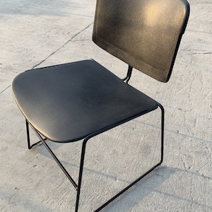 Könnte beinhalten: Ein schwarzer Stuhl mit schlichtem, modernem Design. Der Stuhl hat ein schwarzes Metallgestell und eine schwarze Sitzfläche und Rückenlehne aus Kunststoff.