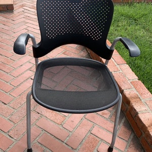 Puede incluir: Silla de oficina de malla negra con patas y brazos de metal plateado. La silla tiene un respaldo perforado y un asiento de malla.