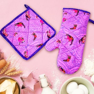 May include: A set of two purple and blue kitchen pot holders with a pink and white floral pattern and raccoon illustrations.