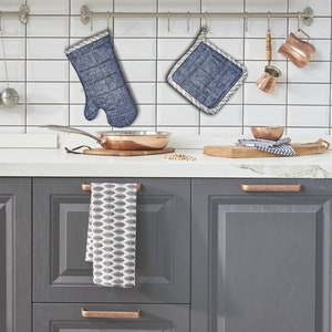 Può includere: Una cucina con armadi grigi e un backsplash di piastrelle bianche. Ci sono due presine blu e bianche appese a ganci, una pentola di rame e una padella di rame sul bancone.