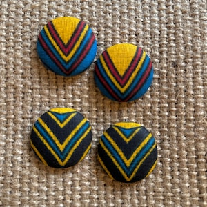 May include: Four fabric covered buttons with a geometric pattern of yellow, red, blue and black stripes.