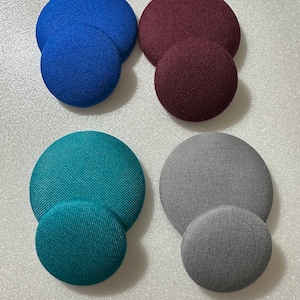 May include: Four pairs of fabric covered buttons in different colors. The buttons are arranged in two rows of two. The top row has a pair of blue buttons and a pair of burgundy buttons. The bottom row has a pair of teal buttons and a pair of gray buttons.