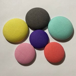 May include: Six round fabric covered buttons in various colors: yellow, gray, light green, purple, pink, and coral.