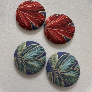 May include: Four fabric covered buttons with a leaf pattern. Two buttons are red with gold accents and two buttons are blue with green and gold accents.