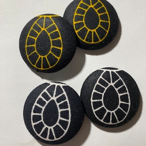 May include: Four fabric buttons with a black background and a white or yellow teardrop-shaped design.