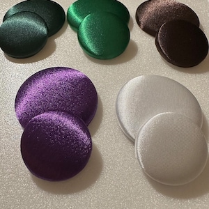 May include: Six pairs of round, fabric covered buttons in various colors. The colors are green, brown, purple, and white.