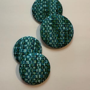 May include: Four round fabric buttons with a teal, green, and white plaid pattern. The buttons are arranged on a light pink background. The buttons are approximately 1.5 inches in diameter.