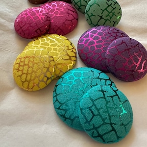 May include: Assortment of nine round fabric buttons with a textured, animal print design. The buttons are in various colors, including teal, purple, pink, yellow, and brown.