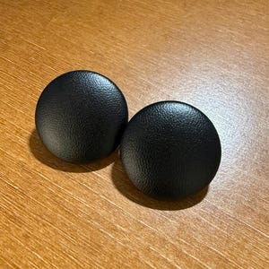 May include: Two black round earrings with a textured surface.