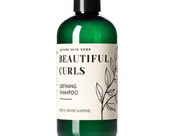 May include: A dark green plastic bottle with a black screw-top cap. The white label features the text NATURE SKIN SHOP, BEAUTIFUL CURLS, DEFINING SHAMPOO, and STEP 2 | INFUSE & DEFINE, accompanied by a black line drawing of a leafy plant stem.
