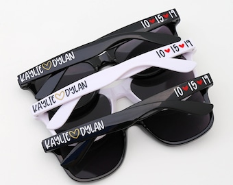 May include: Three pairs of black sunglasses with a white frame. The sunglasses have the text "KAYLIE ♥ DYLAN" printed on the frame and "10 ♥ 15 ♥ 19" printed on the arms.