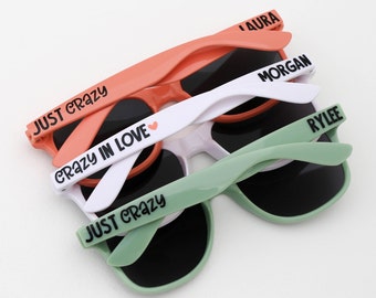 May include: Three pairs of sunglasses with different colored frames and lenses. The top pair is orange with the text "JUST CRAZY" and "CRAZY IN LOVE" on the arms. The middle pair is white with the text "MORGAN" on the arm. The bottom pair is green with the text "JUST CRAZY" and "RYLEE" on the arms.