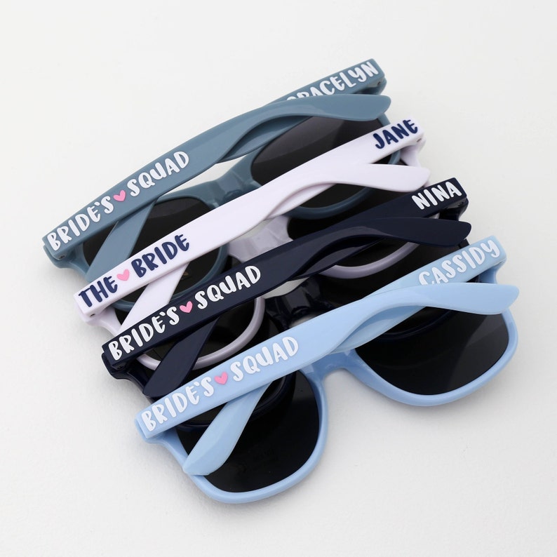 Peut inclure: Ensemble de six lunettes de soleil bleues, blanches et bleu marine avec le texte "Bride's Squad" et "The Bride" sur les branches.