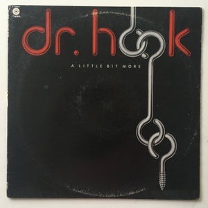 Puede incluir: Una portada de álbum de vinilo negro con el título "dr. hook" en letras rojas y las palabras "A LITTLE BIT MORE" en letras blancas. La portada presenta un diseño de gancho plateado.