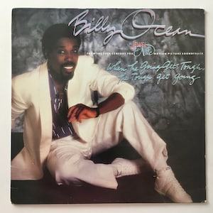 May include: A vinyl record album cover featuring a black man wearing a white suit and sitting on a white surface. The album cover is for the soundtrack to the movie "The Jewel of the Nile" and features the song "When the Going Gets Tough, the Tough Get Going" by Billy Ocean.