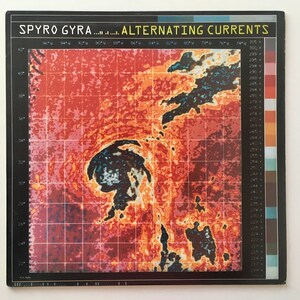 May include: A vintage vinyl record cover for the album "Alternating Currents" by Spyro Gyra. The cover features a red, orange, and yellow color scheme with a black and white image of a hurricane.