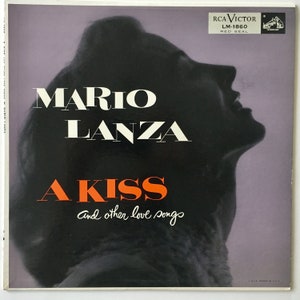 Pode incluir: Uma capa de disco de vinil vintage com uma silhueta em preto e branco da cabeça de uma mulher com o texto "MARIO LANZA A KISS and other love songs" em letras vermelhas e brancas. O rótulo do disco é RCA Victor LM-1860 Red Seal.