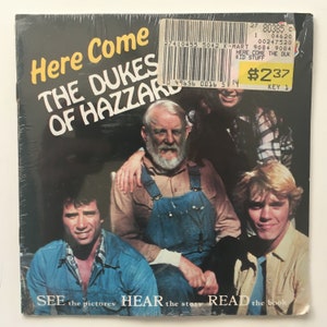 Könnte beinhalten: Ein Buchcover mit einem Foto der Besetzung der Fernsehserie "The Dukes of Hazzard". Der Titel des Buches lautet "Here Come The Dukes of Hazzard". Das Cover enthält auch den Text "See the pictures, Hear the story, Read the book".