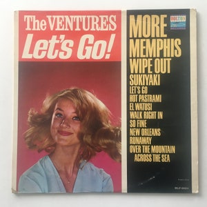May include: A vintage vinyl record album cover featuring The Ventures with the title "Let's Go!" and a photo of a woman with blonde hair. The album title is in red and white text. The album cover is a bright pink color. The album is titled "More Memphis Wipe Out" and lists the songs "Let's Go", "Hot Pastrami", "El Watusi", "Walk Right In", "So Fine", "New Orleans Runaway", "Over The Mountain", and "Across The Sea".