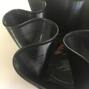 May include: A black vinyl record has been cut and folded into a unique, wavy design. The record is partially visible, showing the grooves and text on the label.