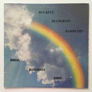 May include: A vintage vinyl record album cover featuring a rainbow against a blue sky with clouds. The album title is "Buckeye Bluegrass Ramblers" and the band name is "Angel Bluegrass Band".