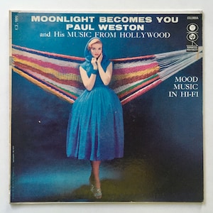 Peut inclure: Une pochette de disque vinyle vintage représentant une femme en robe bleue debout dans un hamac. La pochette est intitulée "Moonlight Becomes You" par Paul Weston et His Music From Hollywood. Le disque est un Columbia LP et est garanti haute fidélité. La pochette comporte également le texte "Mood Music In Hi-Fi."