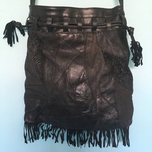 Könnte beinhalten: Schwarze Ledertasche mit Patchwork-Muster, Fransenbesatz und geflochtenem Trageriemen.