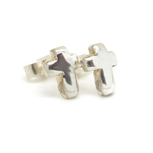 Puede incluir: Un par de pendientes de bot&oacute;n de plata pulida con forma de peque&ntilde;as cruces. Cada pendiente presenta una superficie met&aacute;lica lisa y reflectante con bordes redondeados y un cierre de presi&oacute;n est&aacute;ndar para el l&oacute;bulo de la oreja.