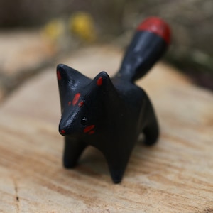 May include: A small black ceramic fox figurine with red accents on its ears, face, and tail. The figurine is standing on a wooden surface.