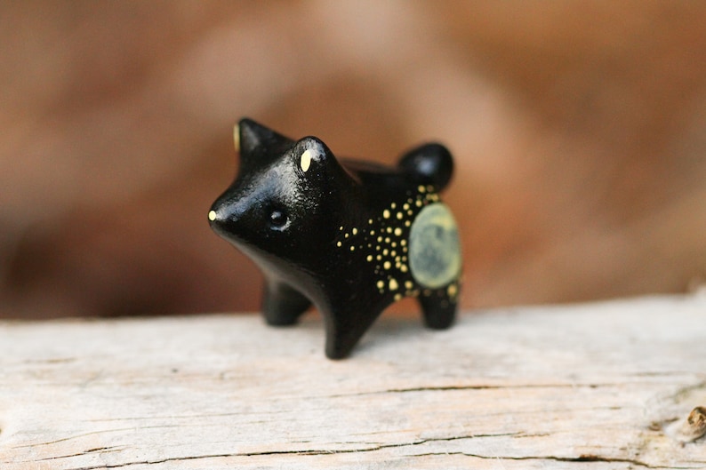 May include: A small black ceramic figurine of a dog with yellow painted spots and a moon on its side.