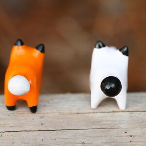 Pu&ograve; includere: Due piccole figurine di animali in ceramica, una arancione con la coda bianca e l'altra bianca con la coda nera. Le figurine sono rivolte con le spalle alla telecamera.