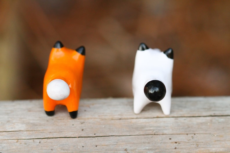 Pu&ograve; includere: Due piccole figurine di animali in ceramica, una arancione con la coda bianca e l'altra bianca con la coda nera. Le figurine sono rivolte con le spalle alla telecamera.
