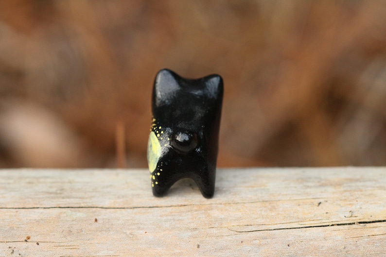 May include: Black ceramic figurine of a dog with yellow and black painted details. The dog is standing on a wooden surface.